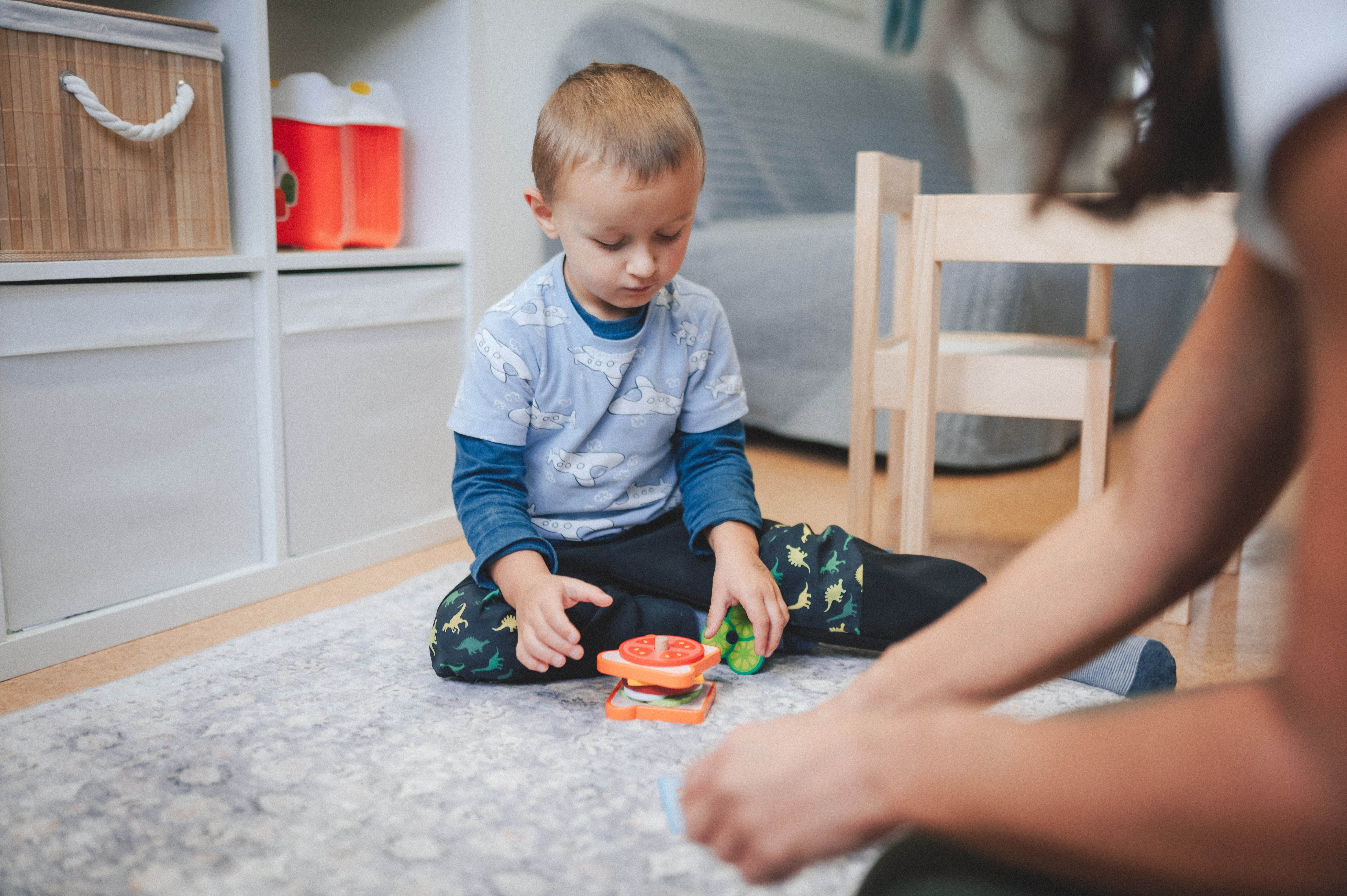 Logopedická terapie s dítětem - chlapec si hraje s hračkovým hamburgerem na koberci při terapii